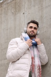 Photo of Handsome man in warm scarf and headphones near wall outdoors