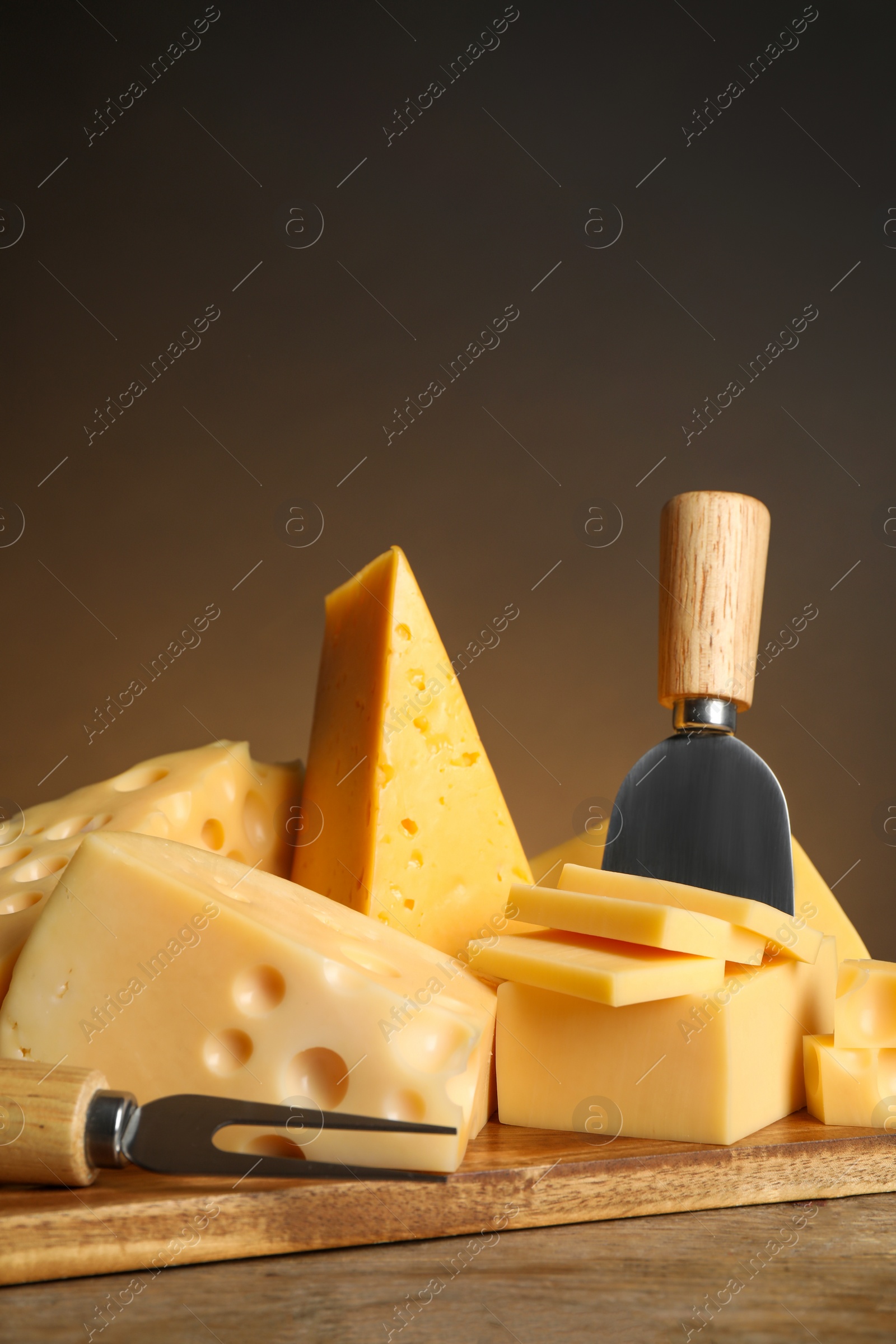 Photo of Different sorts of cheese, fork and knife on wooden table