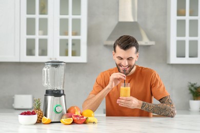 Photo of Handsome man with delicious smoothie at white marble table in kitchen