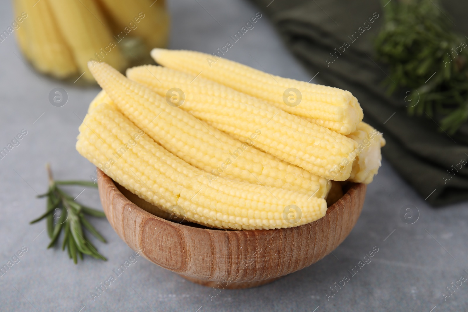 Photo of Tasty fresh yellow baby corns in bowl on grey table