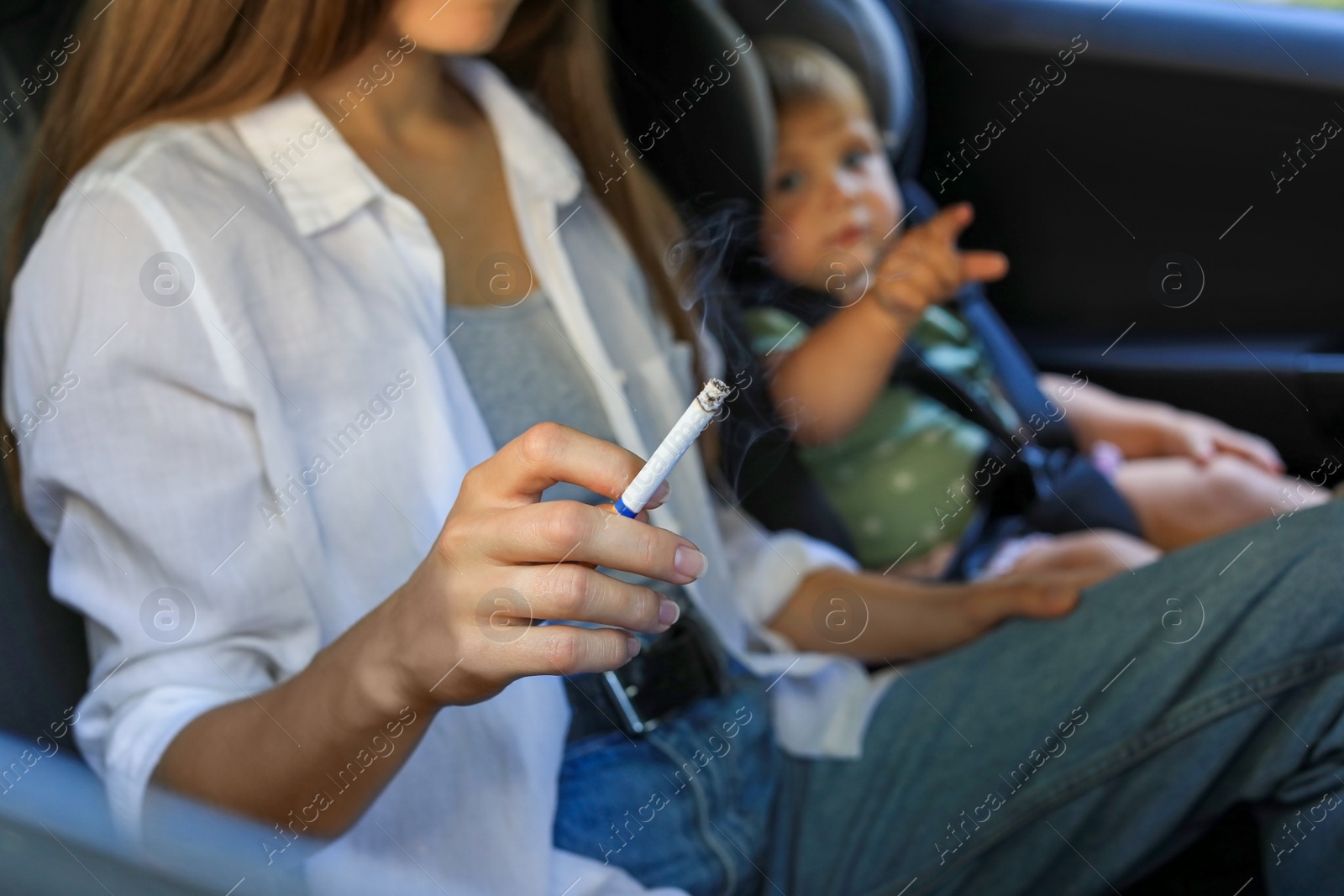 Photo of Mother with cigarette and child in car, closeup. Don't smoke near kids