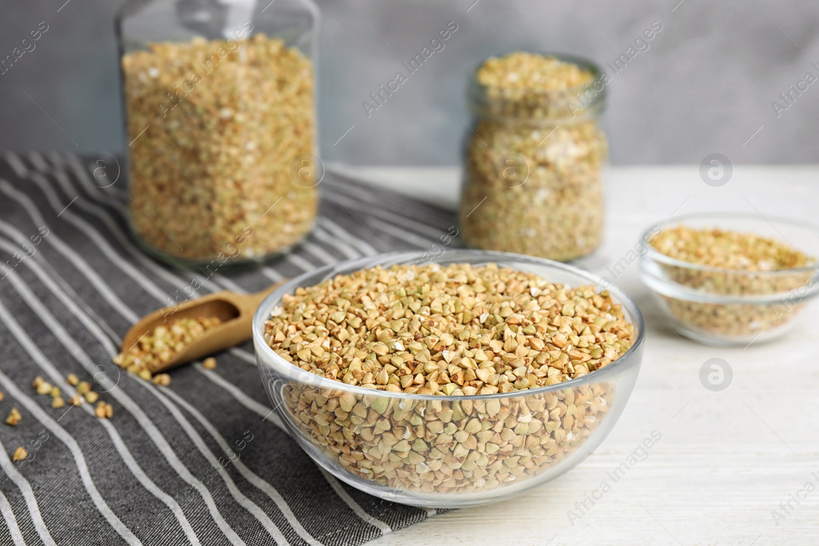 Photo of Uncooked green buckwheat grains in bowl on white wooden table