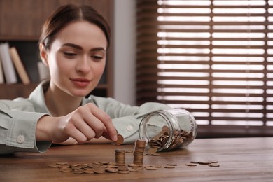 Photo of Woman stacking coins at wooden table indoors