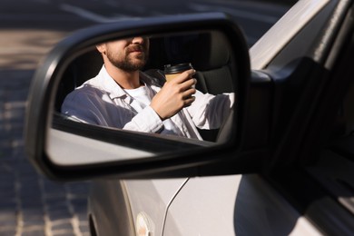 Photo of Coffee to go. Man with paper cup of drink, view through car side mirror