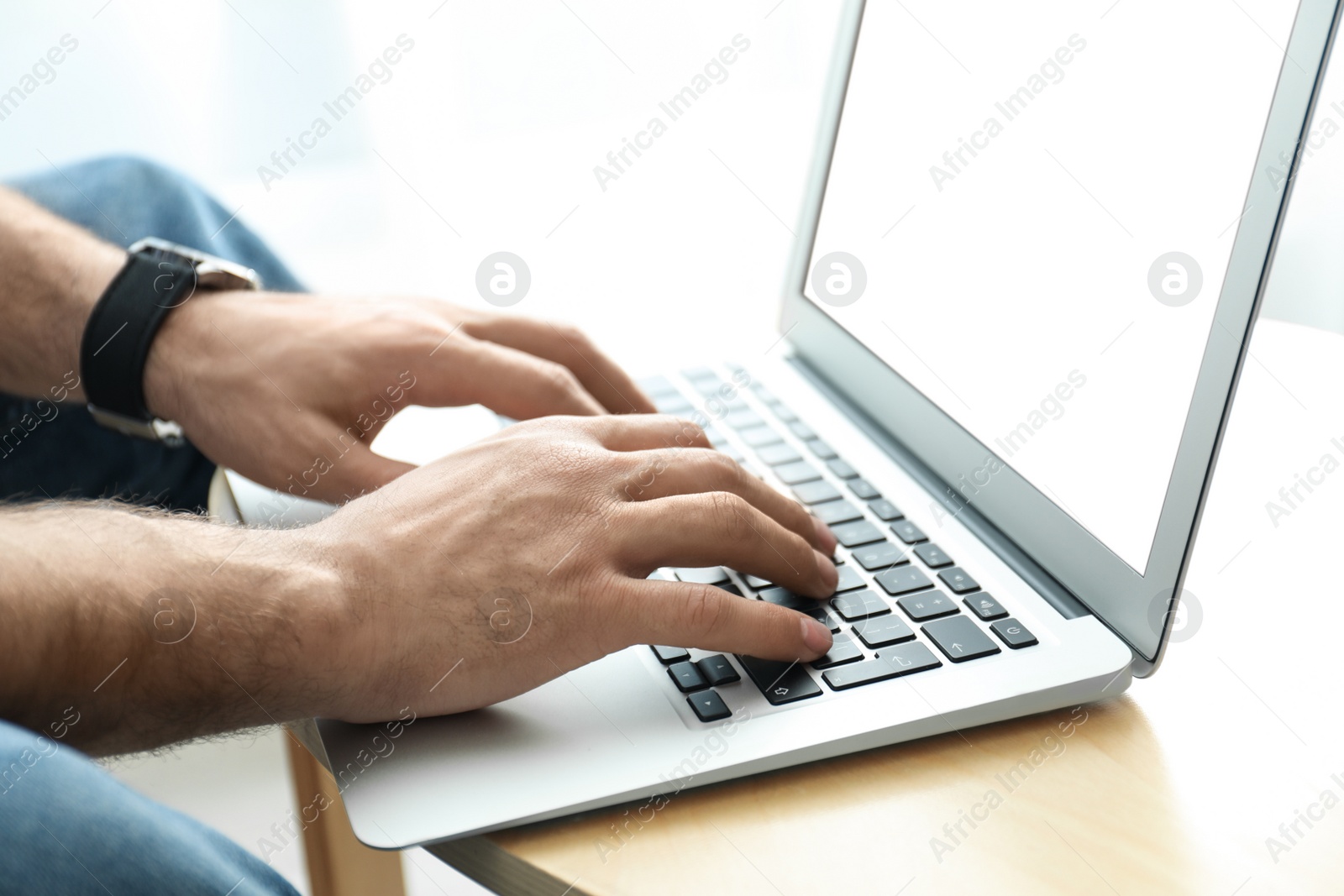 Photo of Man working on modern laptop at wooden table indoors, closeup