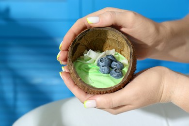 Woman holding coconut shell with tasty smoothie bowl on blurred background, closeup