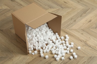 Overturned cardboard box with styrofoam cubes on wooden floor