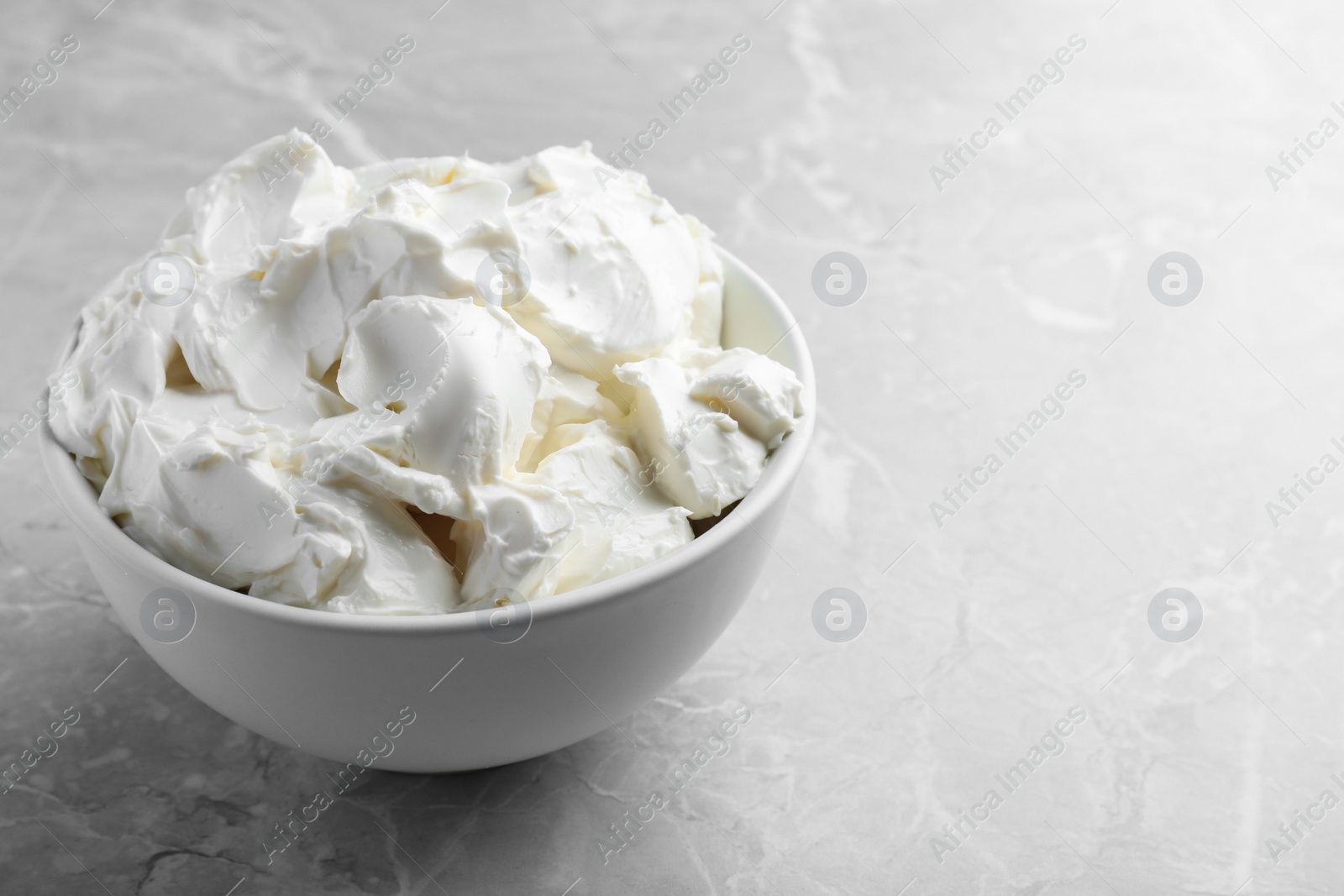 Photo of Bowl of tasty cream cheese on light grey marble table, space for text