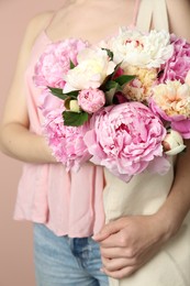 Photo of Woman with bouquet of beautiful peonies in bag on beige background, closeup