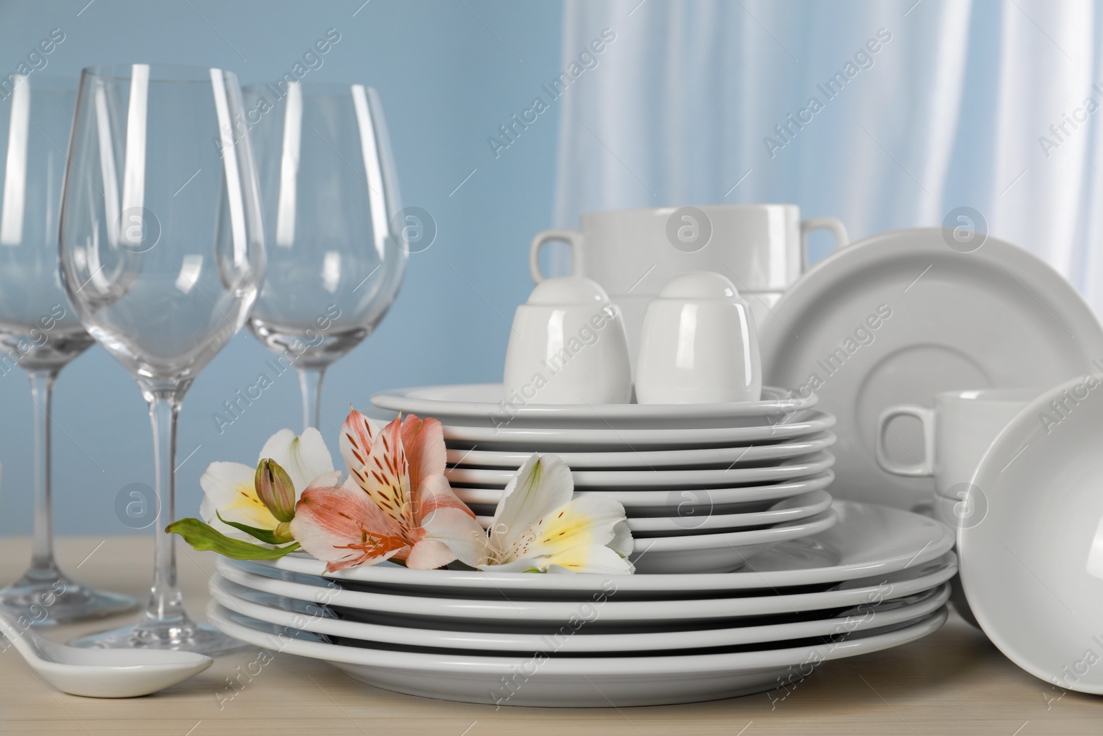 Photo of Glasses and clean dishware with flowers on light grey table