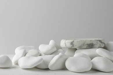 Photo of Presentation for product. Stone podium and white pebbles on table against light background. Space for text