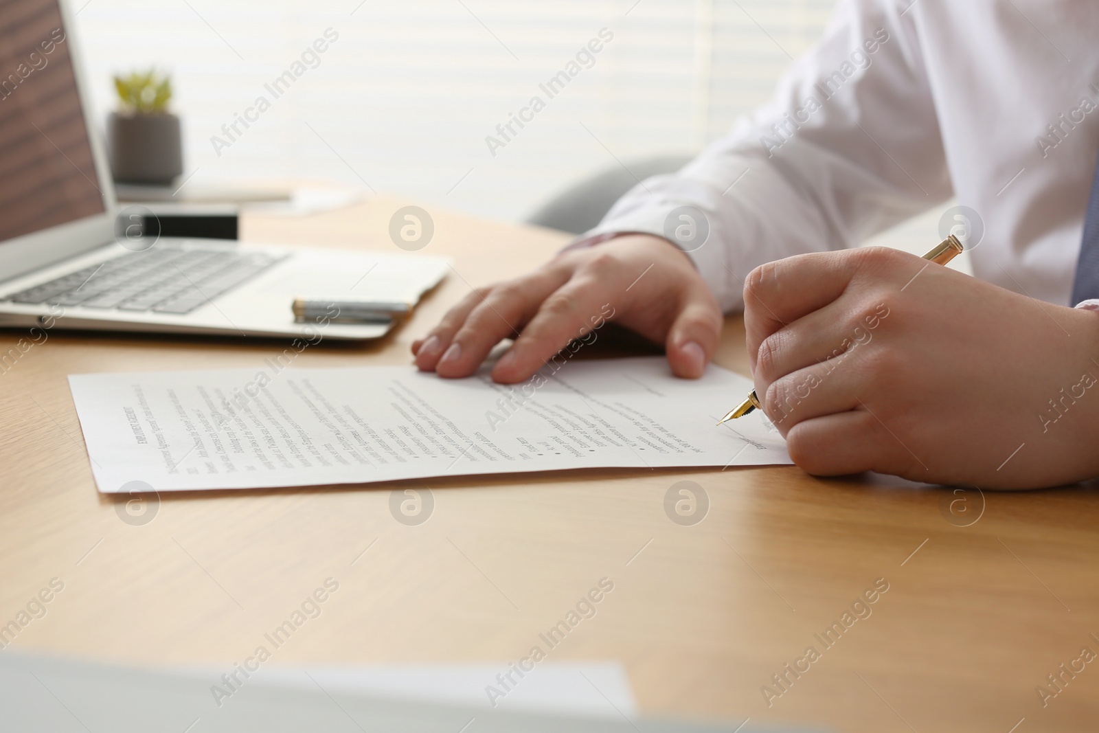 Photo of Notary signing document at wooden table indoors, closeup