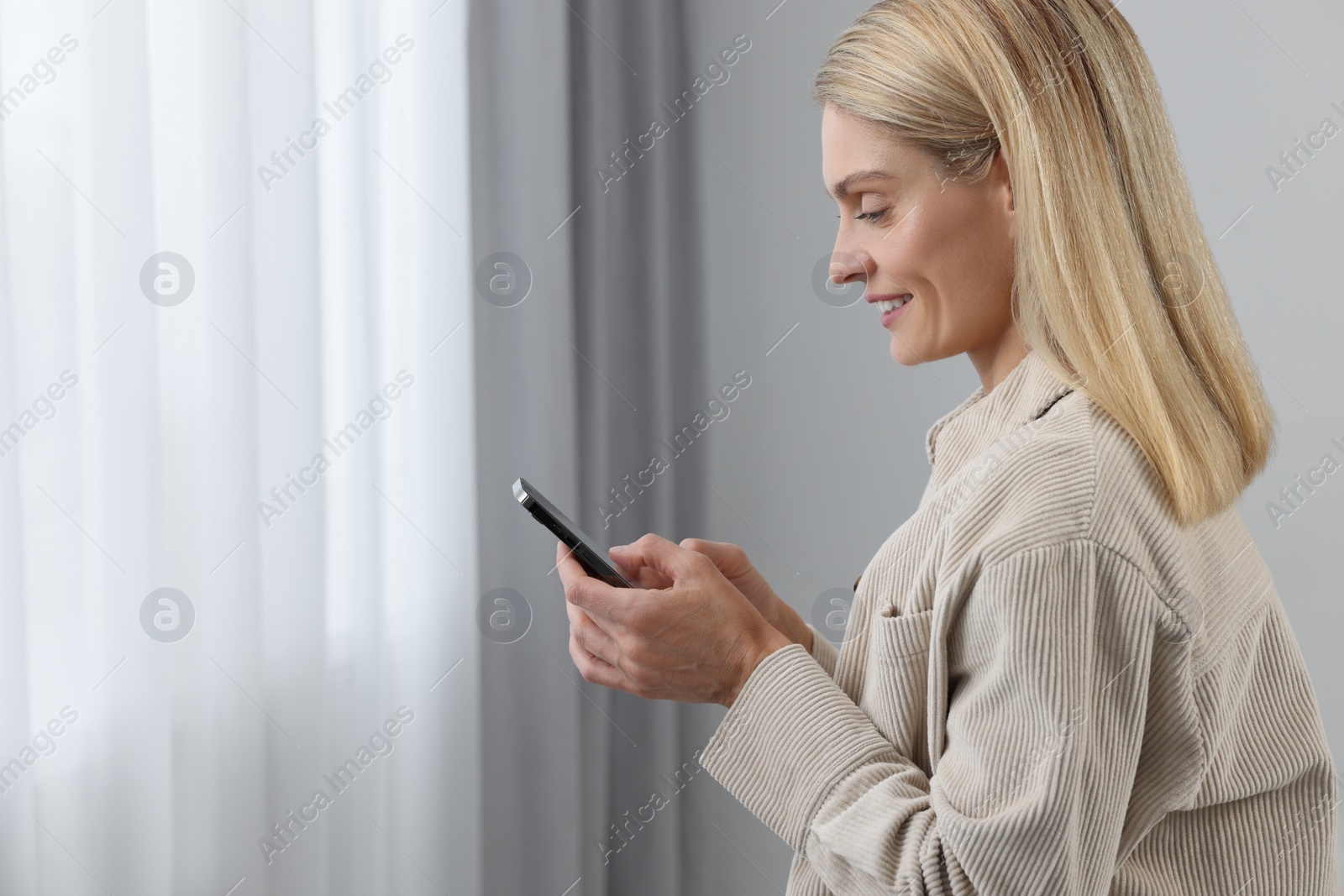 Photo of Happy woman sending message via smartphone at home, space for text