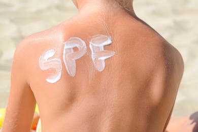 Photo of Child with abbreviation SPF of sunscreen on back at beach, closeup