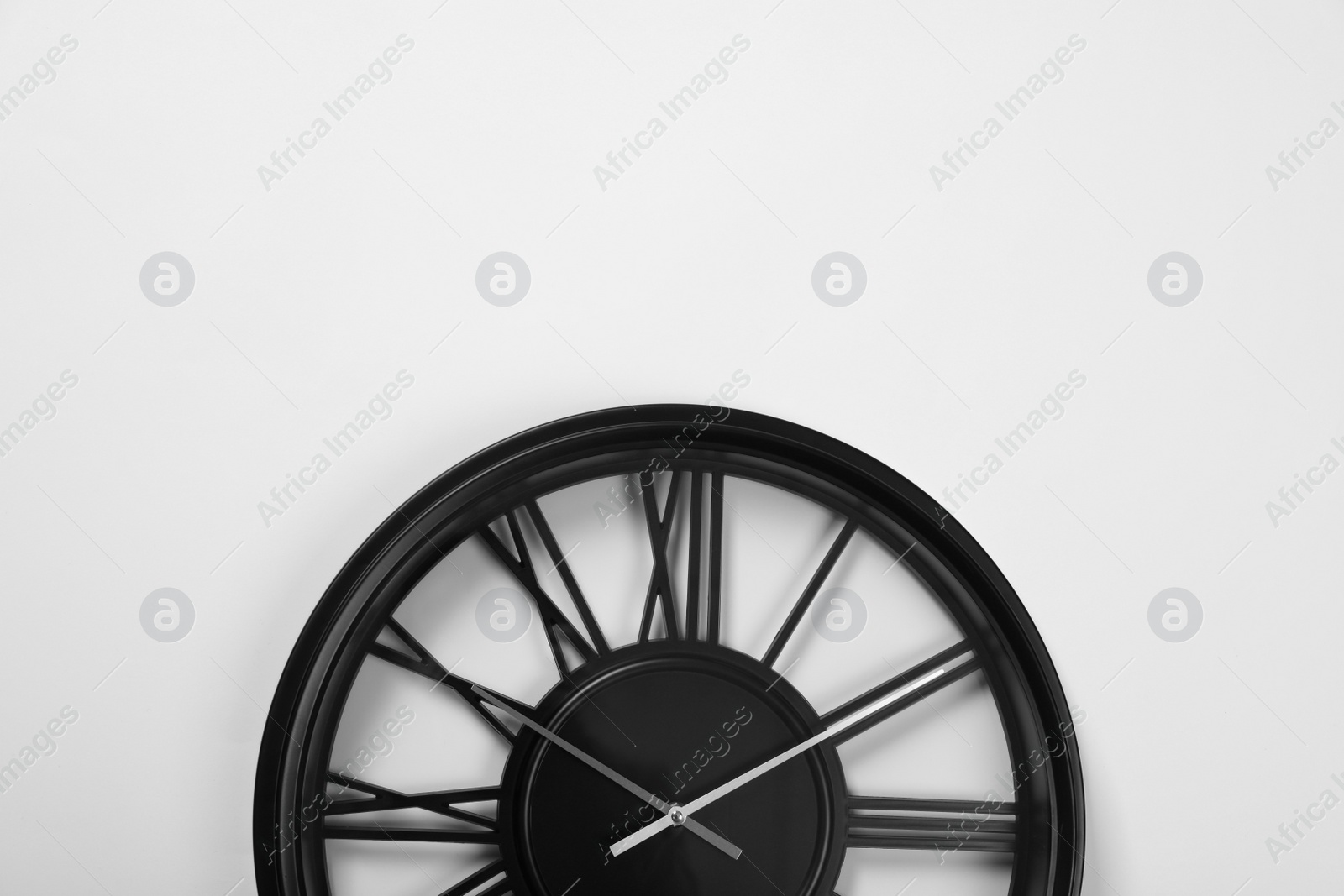 Photo of Stylish analog clock hanging on white wall, space for text