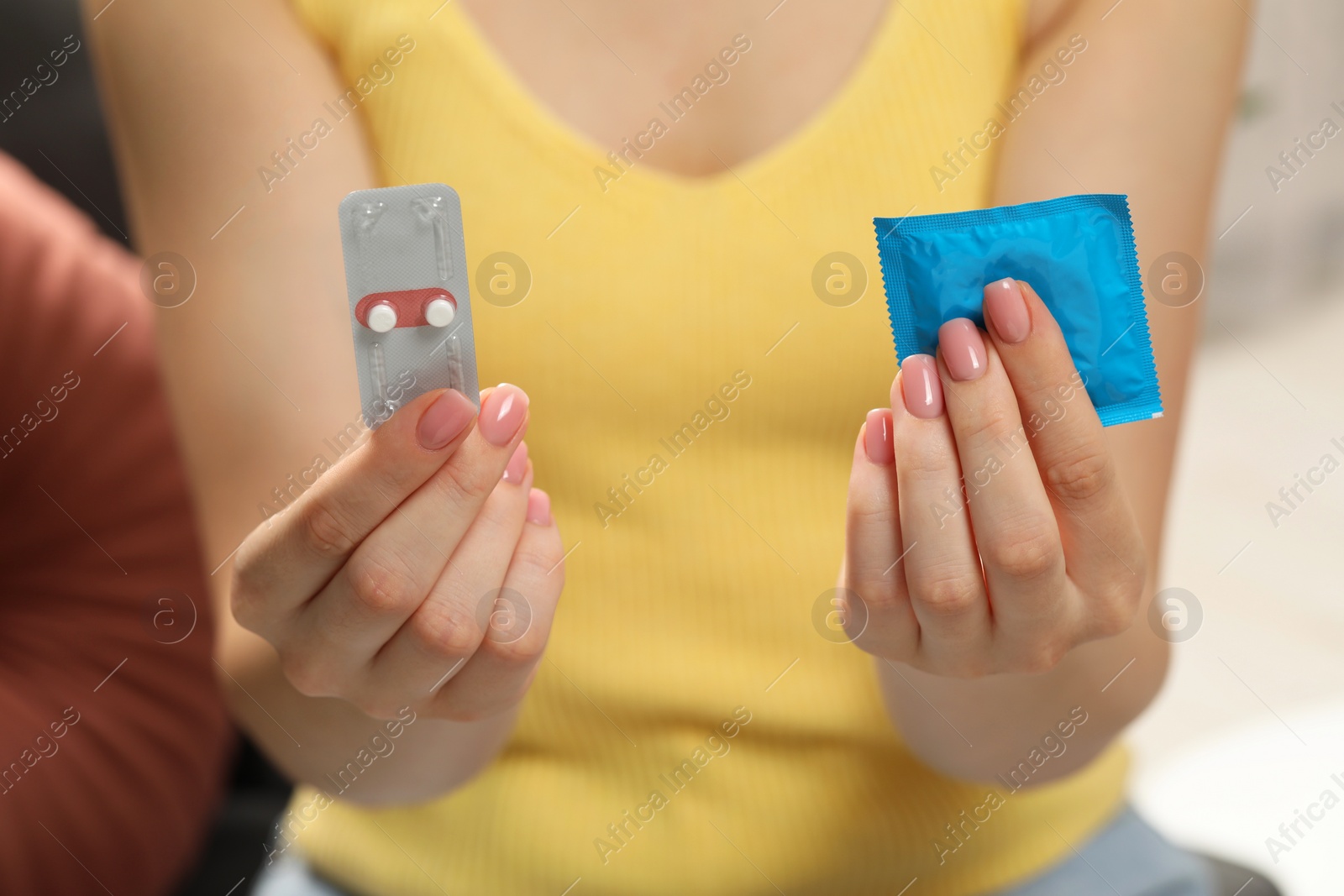 Photo of Woman holding condom and contraceptive pills on blurred background, closeup. Choosing birth control method