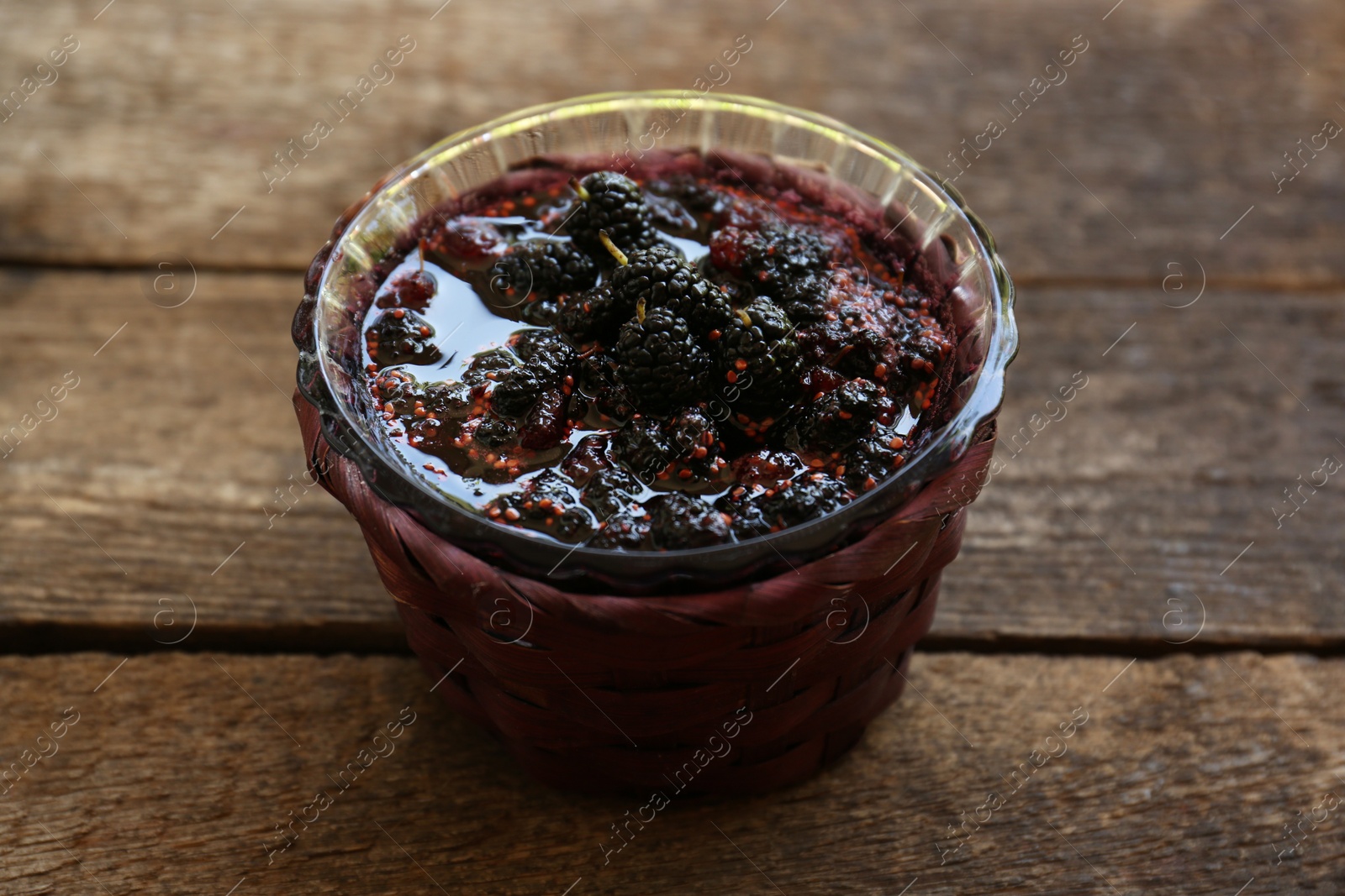 Photo of Bowl of sweet black mulberry jam on wooden table