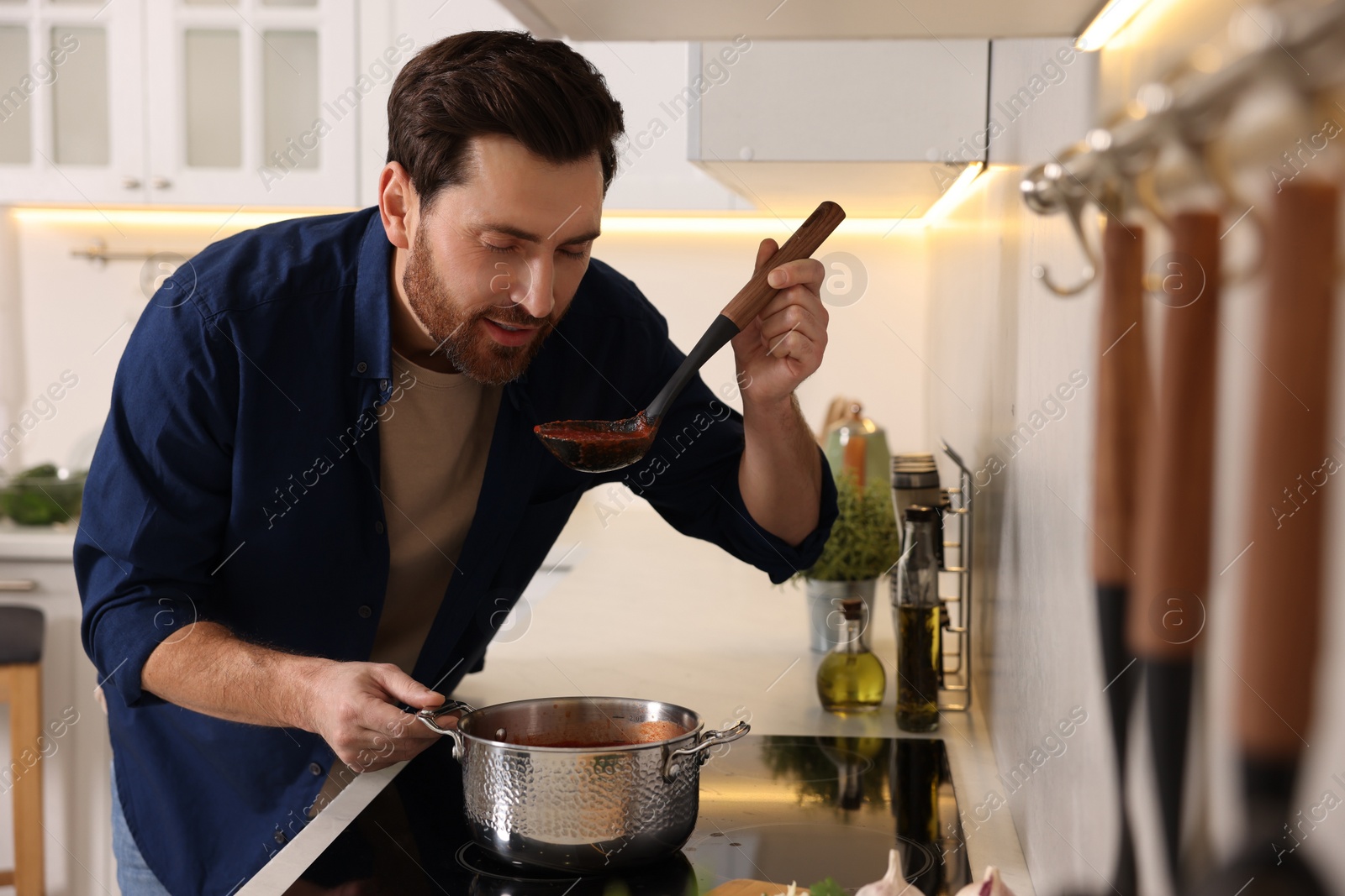 Photo of Man tasting delicious tomato soup in kitchen