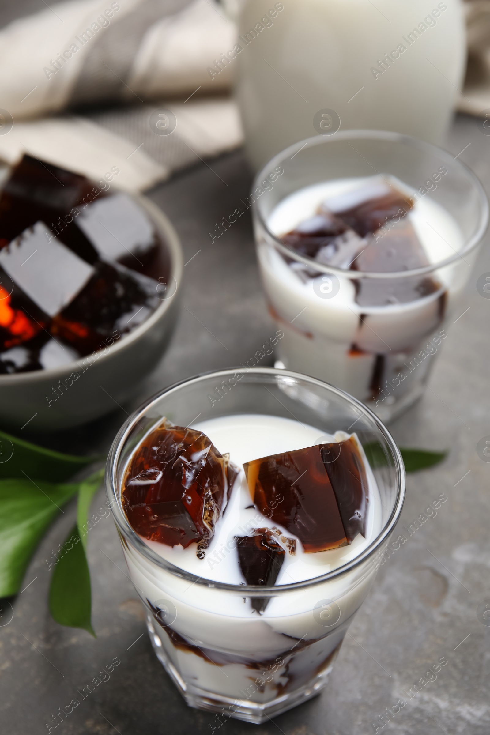 Photo of Glasses of milk with delicious grass jelly on grey table, closeup