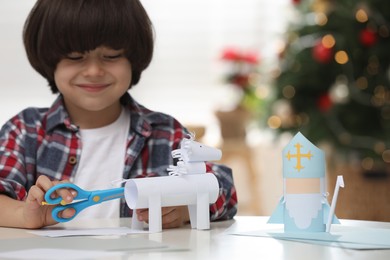 Cute little boy making paper toy for Saint Nicholas day at home, focus on hands