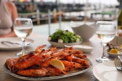 Photo of Plate of delicious cooked shrimps served with lemon and wine at table outdoors