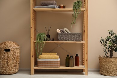 Photo of Shelving unit with soft towels, plants and bottles indoors