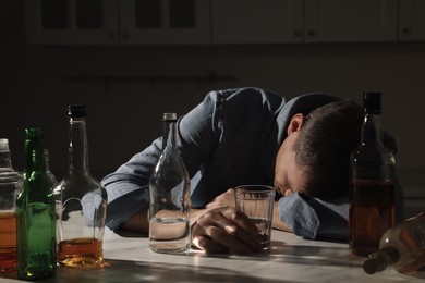 Photo of Addicted man with alcoholic drink sleeping at table in kitchen