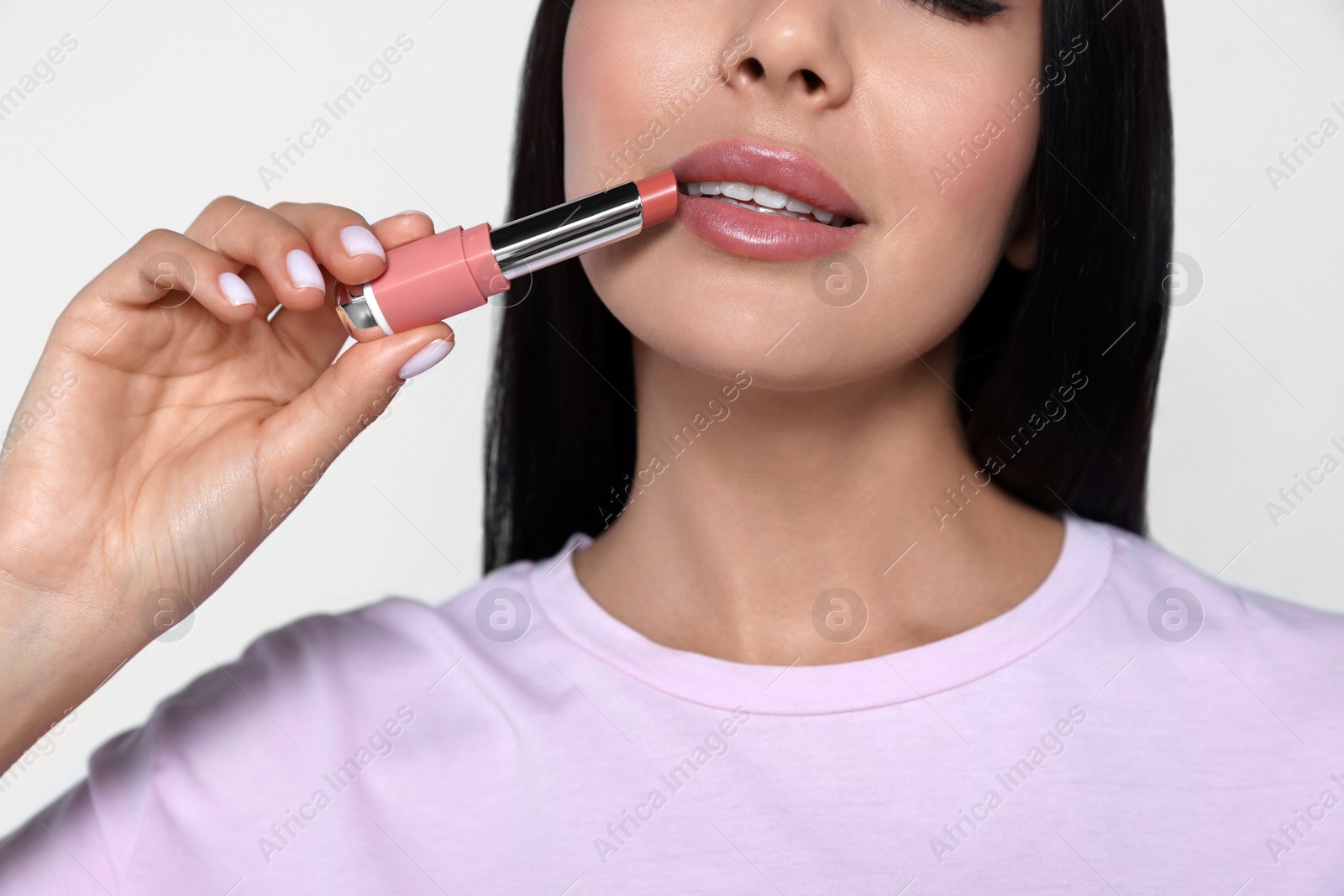 Photo of Young woman with beautiful makeup holding nude lipstick on light gray background, closeup