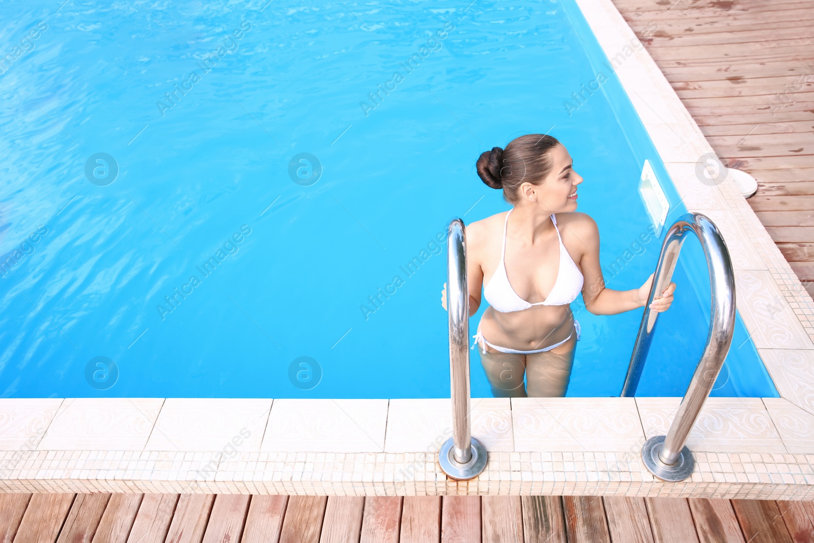 Photo of Beautiful young woman in bikini standing near pool stairs, outdoors