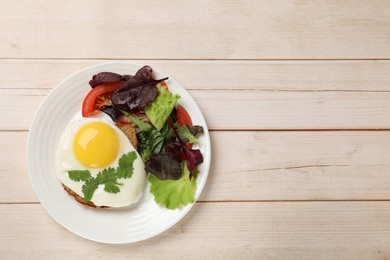 Photo of Plate with tasty fried egg, slice of bread and salad on light wooden table, top view. Space for text