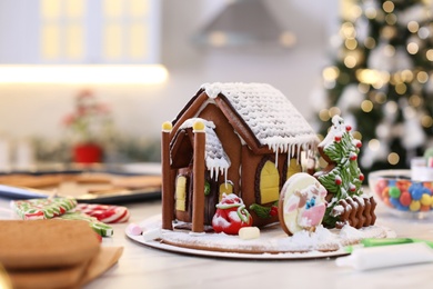 Photo of Beautiful gingerbread house decorated with icing on white table indoors