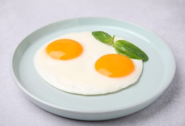 Tasty fried eggs with basil in plate on white table, closeup