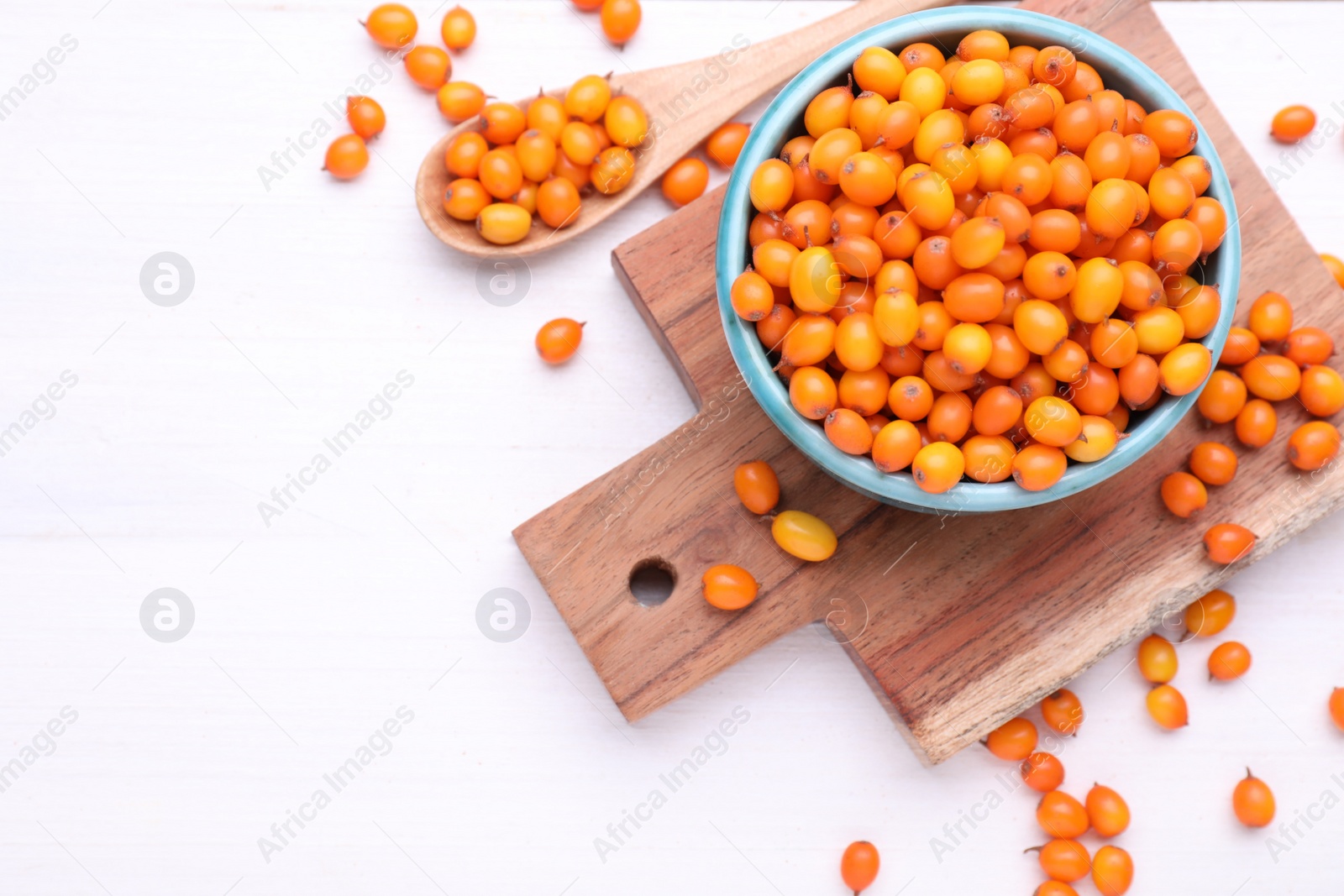 Photo of Bowl and spoon with fresh ripe sea buckthorn berries on white wooden table, flat lay. Space for text