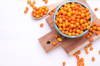 Bowl and spoon with fresh ripe sea buckthorn berries on white wooden table, flat lay. Space for text