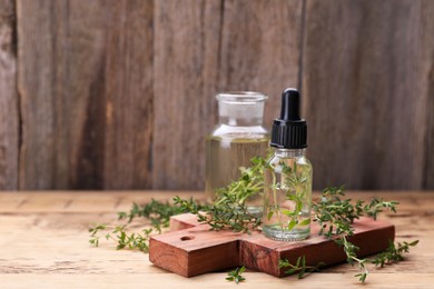 Photo of Bottles of thyme essential oil and fresh plant on wooden table, space for text