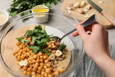 Photo of Woman mixing ingredients for delicious hummus at light grey table, closeup