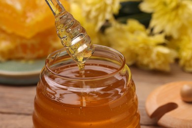 Pouring sweet golden honey from dipper into jar at table, closeup