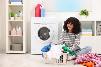 Happy woman with laundry near washing machine indoors