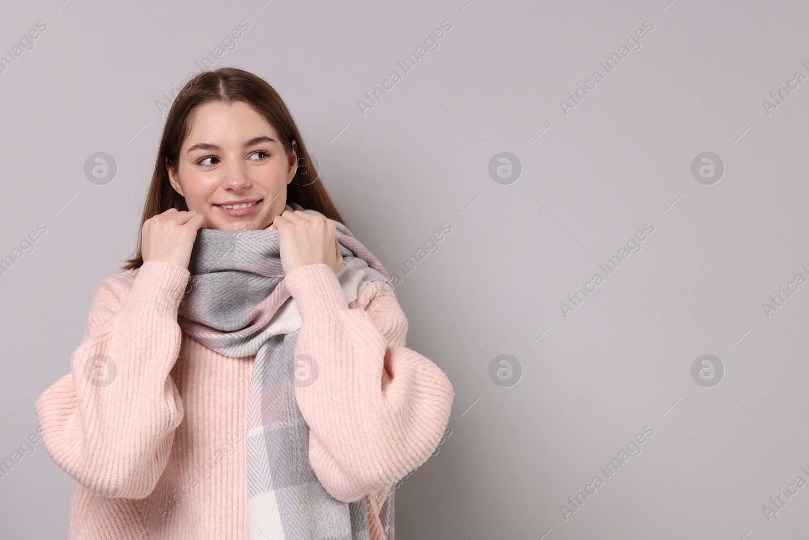 Photo of Beautiful woman in warm scarf on gray background, space for text