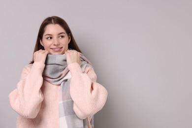 Beautiful woman in warm scarf on gray background, space for text