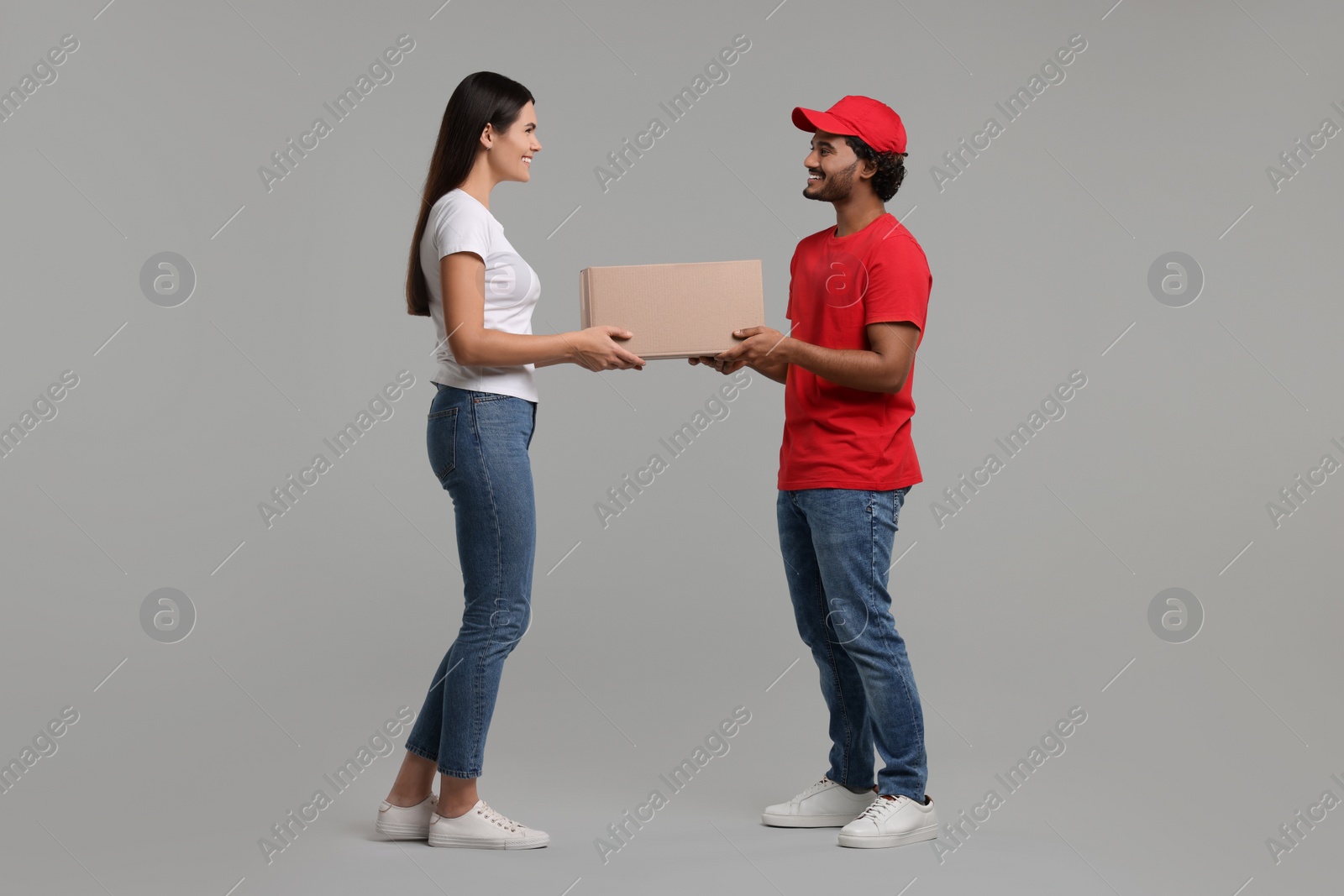 Photo of Smiling courier giving parcel to receiver on grey background