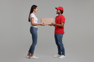 Photo of Smiling courier giving parcel to receiver on grey background