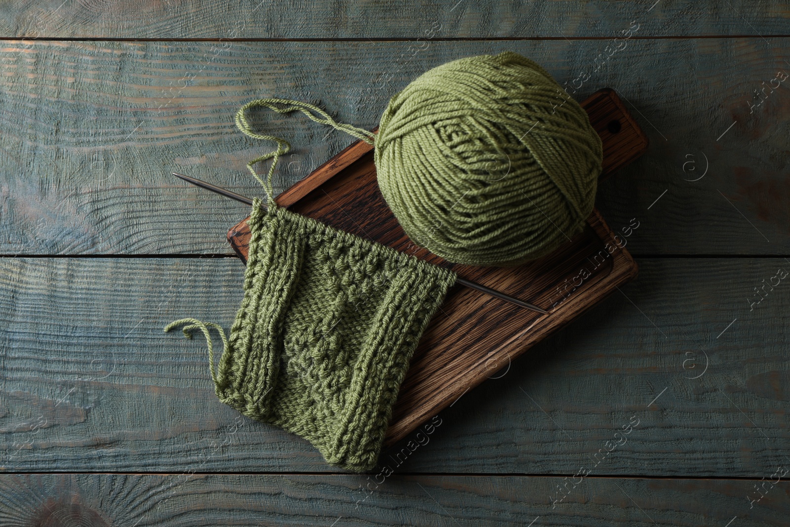 Photo of Soft yarn, knitting and metal needle on light blue wooden table, top view