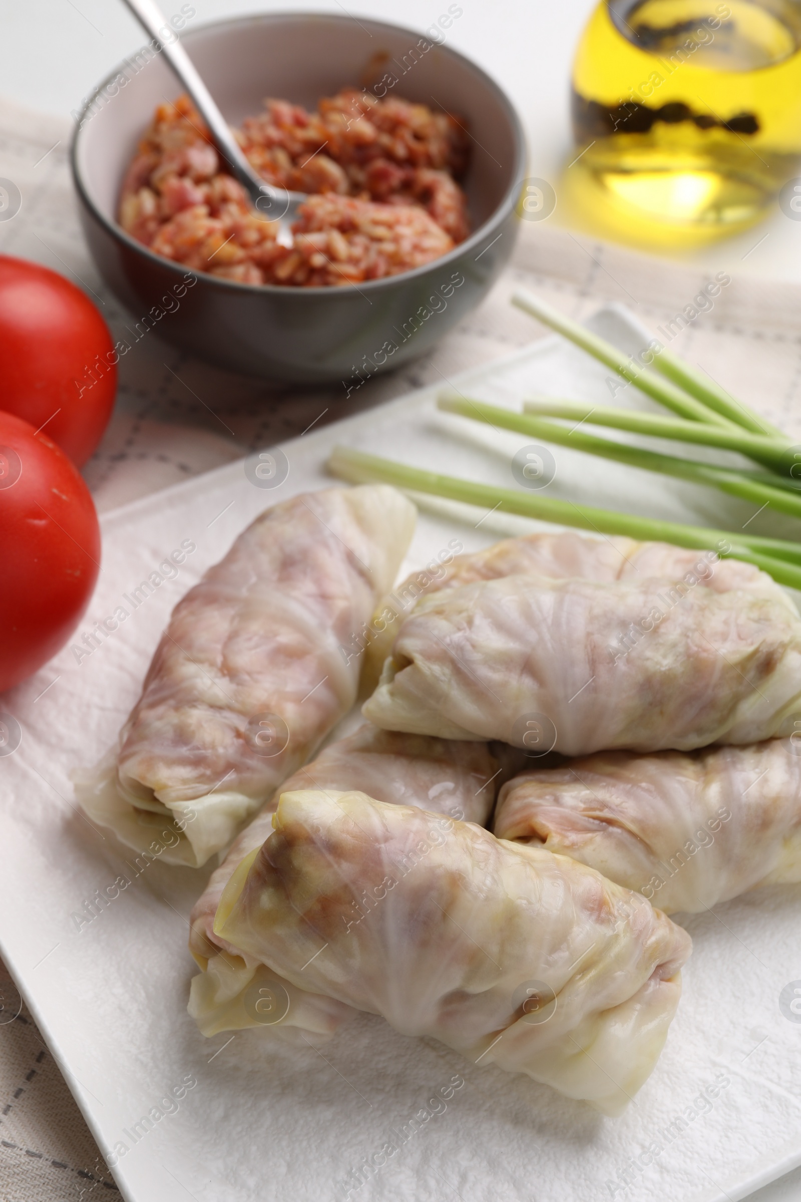 Photo of Uncooked stuffed cabbage rolls and ingredients on table, closeup