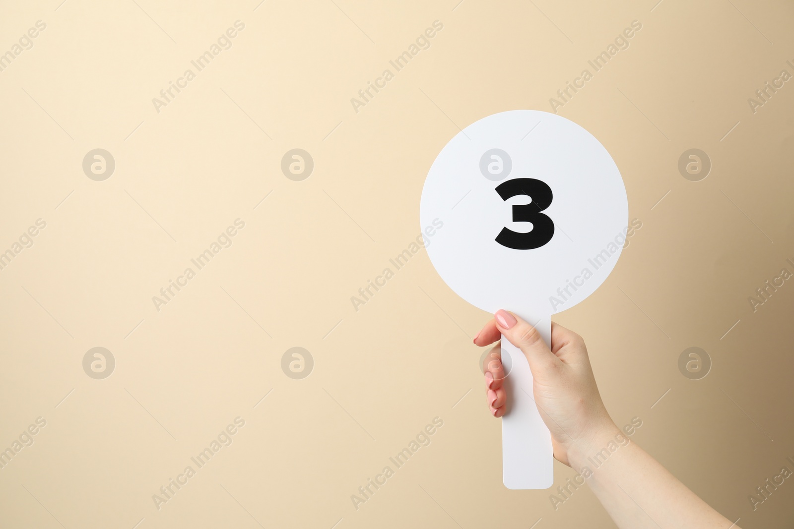 Photo of Woman holding auction paddle with number 3 on beige background, closeup. Space for text