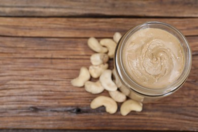 Photo of Tasty cashew nut paste in jar on wooden table, top view. Space for text