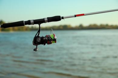 Photo of Fishing rod with reel near river, space for text