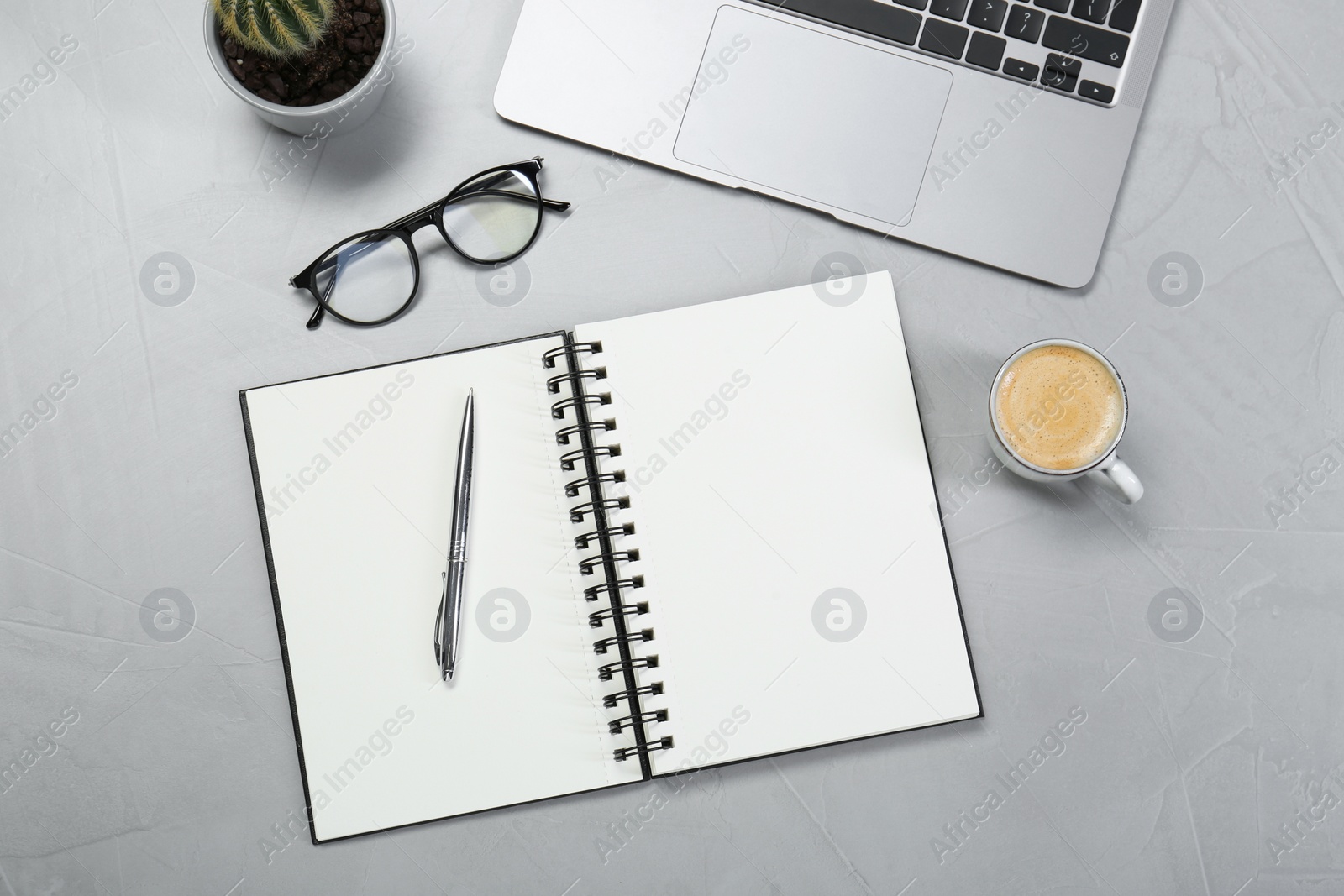 Photo of Open notebook, laptop, coffee and pen on light grey table, flat lay