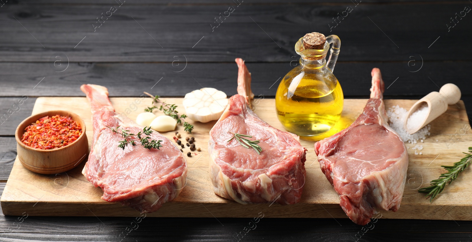 Photo of Fresh tomahawk beef cuts, spices and oil on black wooden table