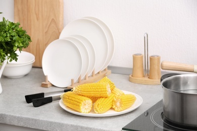 Photo of Plate with ripe corn cobs and tongs on kitchen table